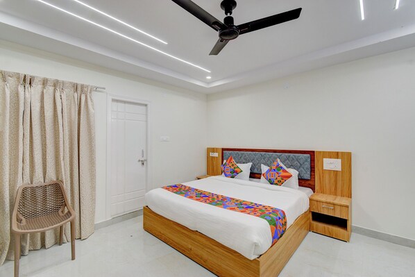A bedroom with a bed, wooden headboard, bedside tables, a ceiling fan, and a chair. - FabHotel Dharani Grand Madhapur - Image Gardens & Metro, Madhapur (Hyderabad)