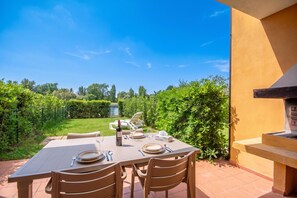 An outdoor dining area with a table set for four, surrounded by greenery and a clear sky. - Albarella S4 1, Isola di Albarella, Italy (Isola di Albarella)