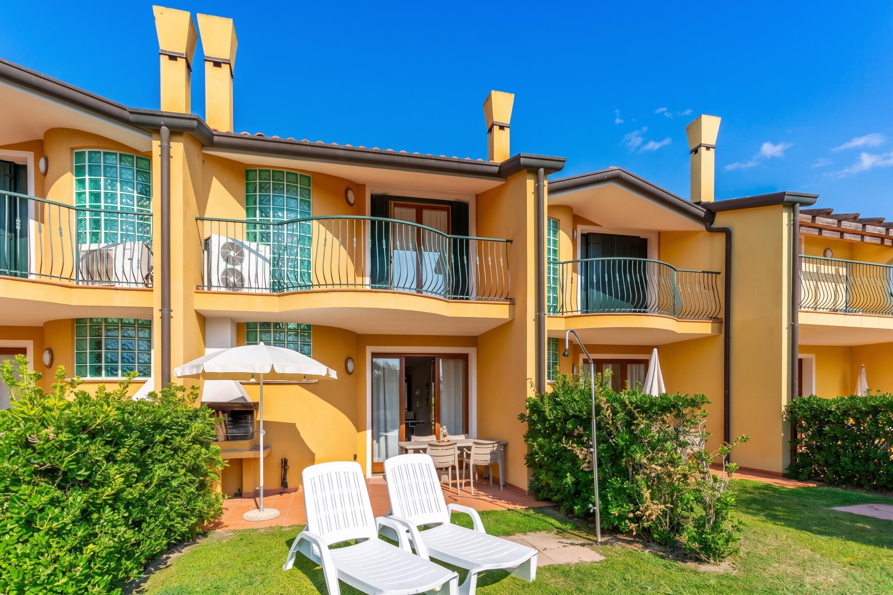 A two-story building with balconies, a patio with chairs, and a small table.