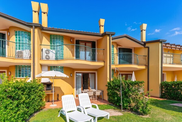 A two-story building with balconies, a patio with chairs, and a small table. - Albarella S4 1, Isola di Albarella, Italy (Isola di Albarella)