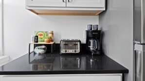 A kitchen with a black countertop, a toaster, a coffee maker, and a cabinet above. - Close To Downtown | Luxury Getaway Apartment In Midtown (Detroit)