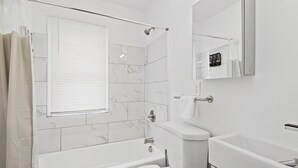 A modern bathroom with a bathtub, toilet, and a large mirror. - Close To Downtown | Luxury Getaway Apartment In Midtown (Detroit)