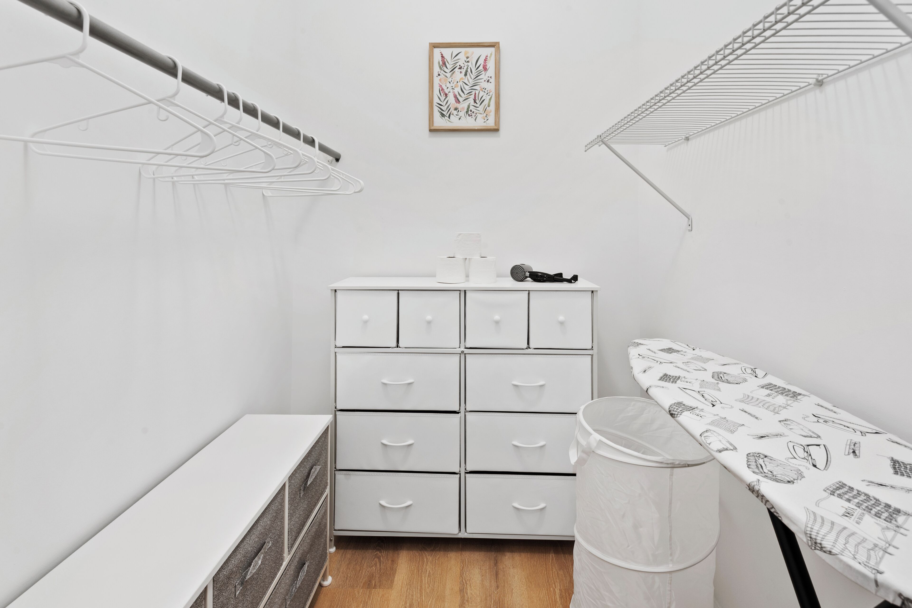 Une pièce compacte et blanche, dotée d’une armoire intégrée, d’une petite table avec une poubelle et d’un étendoir fixé au mur.