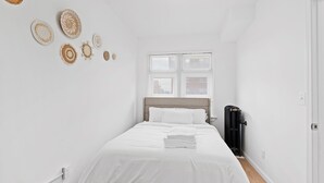 A neatly arranged bedroom with a bed, white bedding, a radiator, and a window with blinds. - Close To Downtown | Luxury Getaway Apartment In Midtown (Detroit)