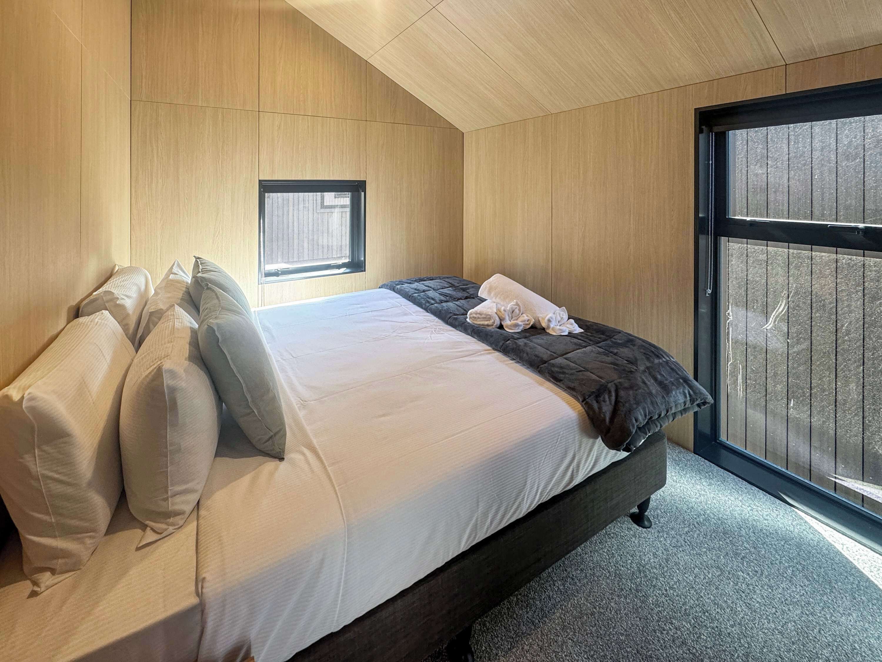 Ein Schlafzimmer mit einem Bett, Kissen, einem Fenster und Blick nach draußen.