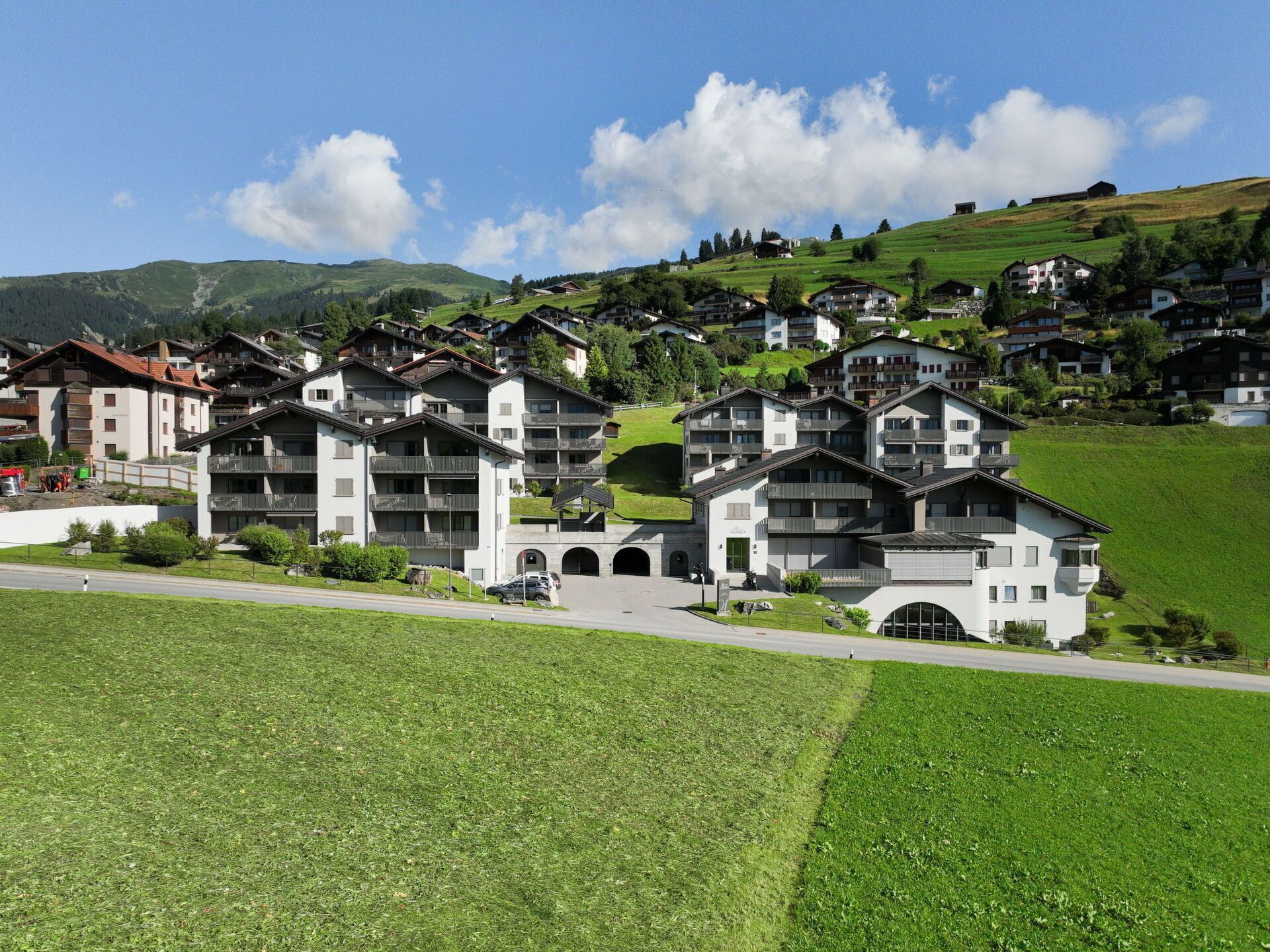 Un gruppo di edifici moderni a più piani con balconi, sullo sfondo di colline verdi e un cielo sereno.