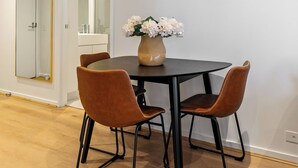 A dining area with a round table, two brown leather chairs, and a vase with flowers. - Modern 1BR Prima Tower • Walk to Crown (Melbourne)