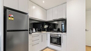 A modern kitchen with white cabinetry, a stainless steel refrigerator, a built-in oven, and a black range hood. - Modern 1BR Prima Tower • Walk to Crown (Melbourne)