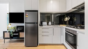 A modern kitchen with a built-in refrigerator, a stove, and a microwave. There is a dining area with a table and chairs, and a TV mounted on the wall. - Modern 1BR Prima Tower • Walk to Crown (Melbourne)