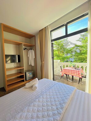 A bedroom with a bed, a TV, a minibar, and a balcony with a table and chairs. - New City Homestay - Grand World Phu Quoc (Phu Quoc)