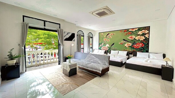 Une chambre spacieuse avec un grand lit, un canapé-lit et une vue sur un balcon aménagé avec du mobilier d’extérieur.