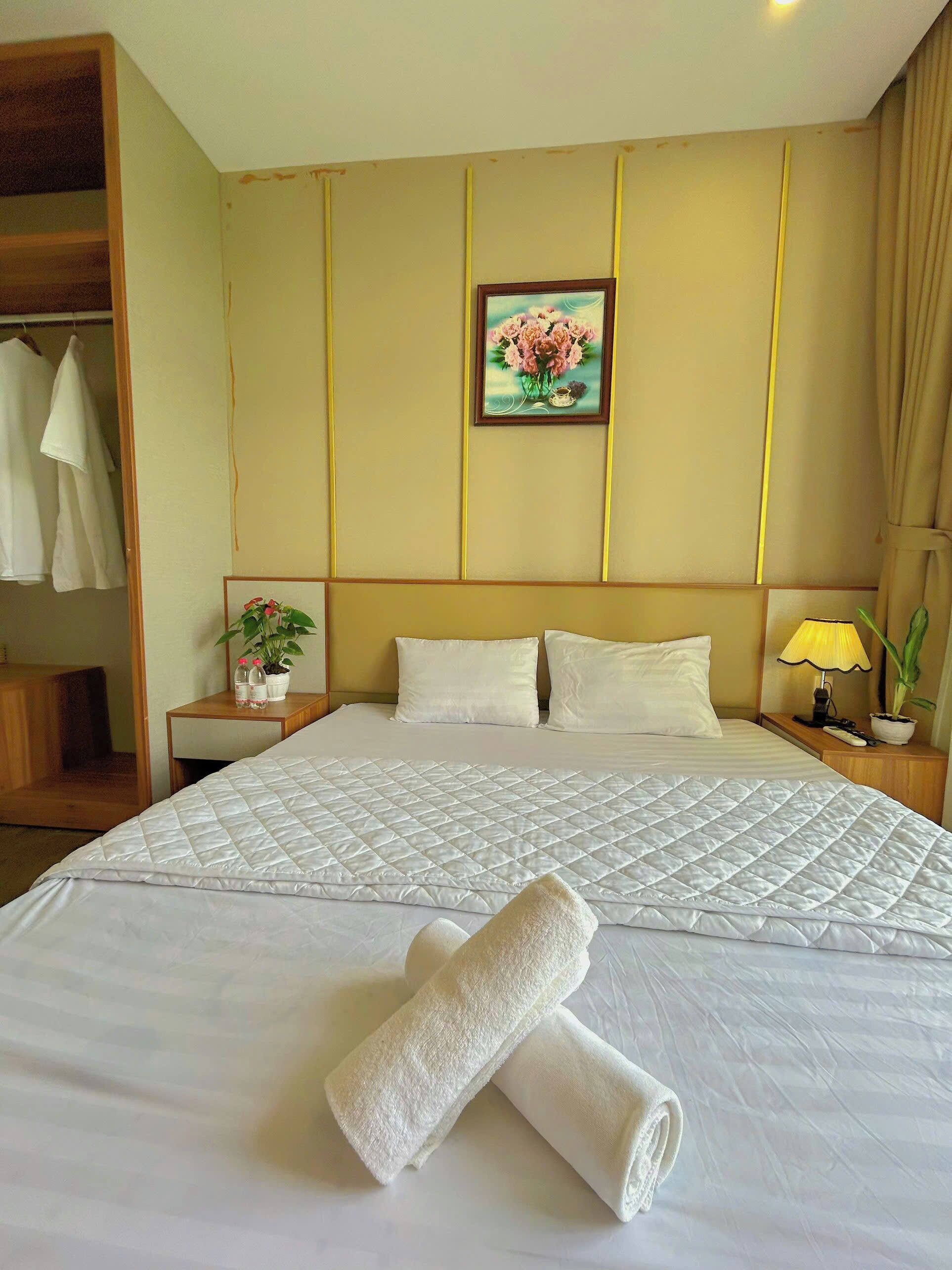 Ein Hotelzimmer mit einem großen Bett, einem Nachttisch mit Lampe, einem Beistelltisch mit Pflanze und einem Kleiderschrank.