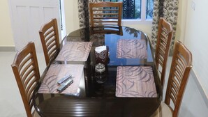 Un coin repas avec une table ronde, six chaises en bois, des coussins à motifs et un vase décoratif.
