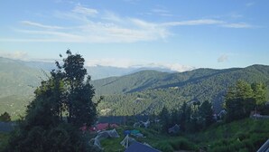 Un paysage montagneux sous un ciel dégagé. On y voit plusieurs maisons avec des toits bien visibles, ainsi que de la végétation alentour.
