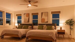 Ein Schlafzimmer mit zwei Betten, einem Deckenventilator, Nachttischlampen und einer Topfpflanze.