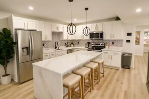 A modern kitchen with white cabinets, a large island with bar stools, stainless steel appliances, and a patterned backsplash. - Modern 4BR Sleeps 13 with Rooftop 4 Bathrooms Garage Near PNC Park (Pittsburgh)