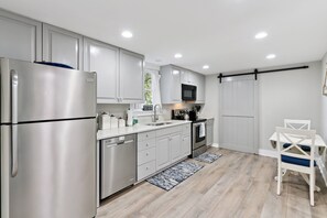 A modern kitchen with stainless steel appliances, white cabinetry, and a dining area with a white table and chairs. - NEW LISTING! Seabreeze Cottage | Charming St. Simons Island Beach Cottage Near Pier Village (Saint Simons Island)