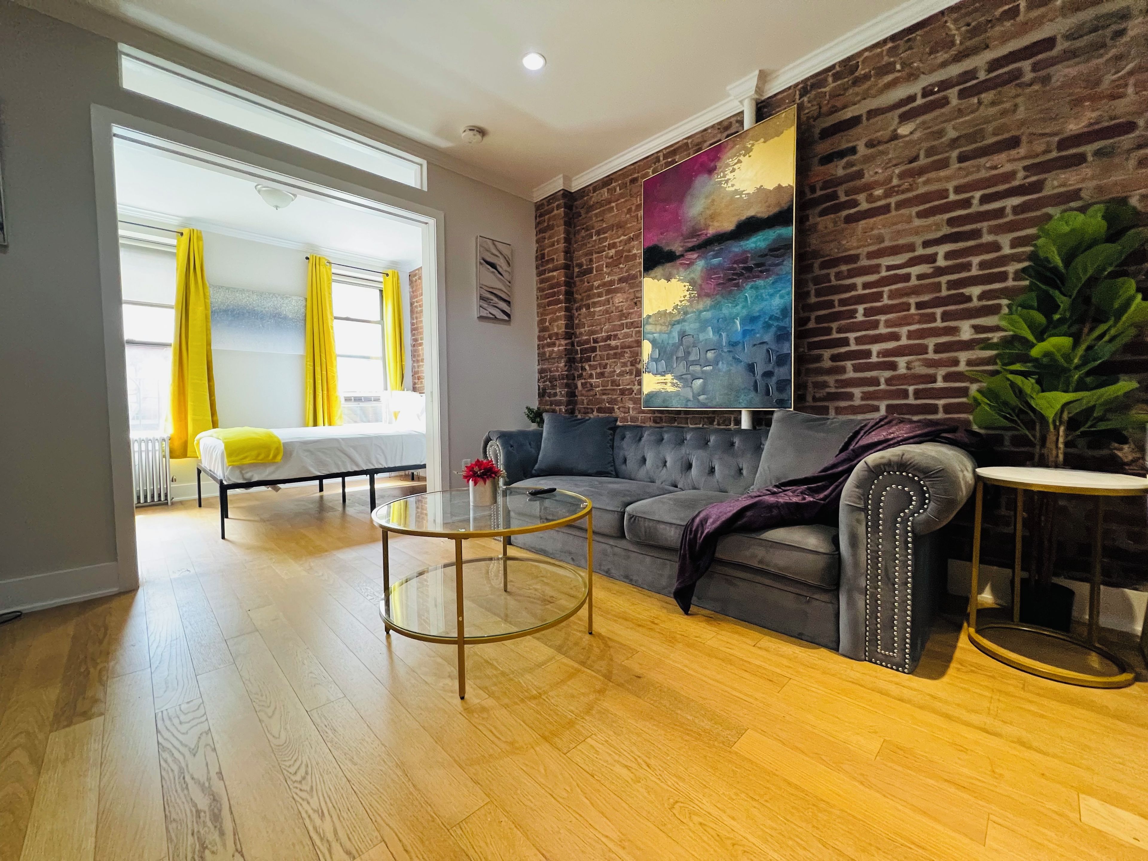 A modern living room with a sofa, a glass coffee table, and a brick wall.