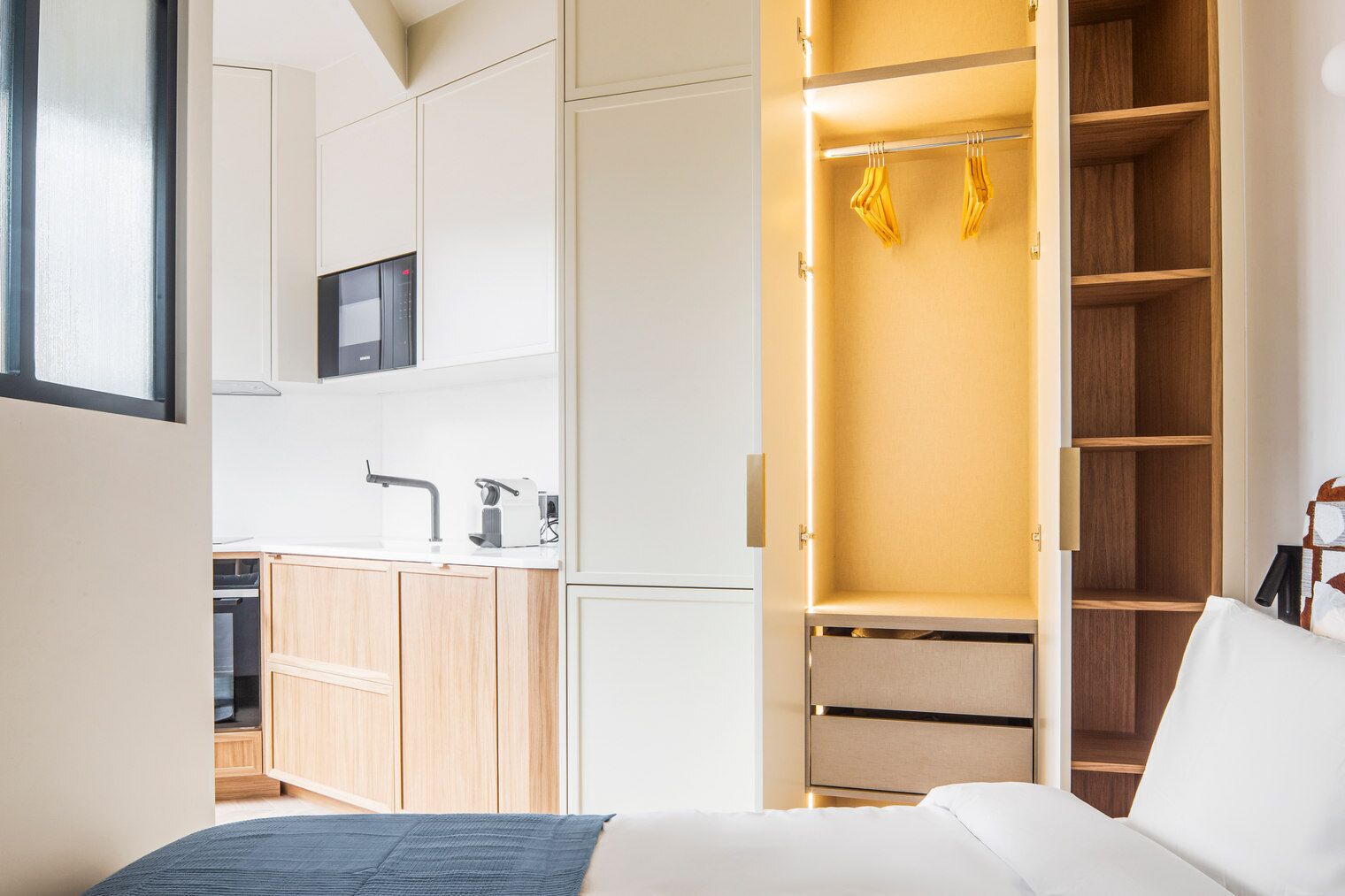 Ein modernes Hotelzimmer mit Bett, integriertem Kleiderschrank, einer Küchenzeile und einem Badezimmer.