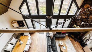 Una habitación espaciosa con techo de vigas de madera, chimenea de piedra y un amplio ventanal con vistas al exterior.