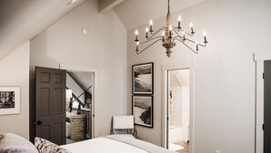 Un dormitorio con una cama grande, una araña, un armario y una escalera que conduce a otra habitación.