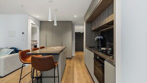 Eine moderne Küche mit einer zentralen Kochinsel, Barhocker und einem Essbereich mit einer Couch und Sesseln.