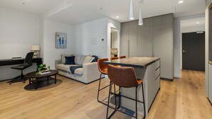 Eine moderne Küche mit einer zentralen Kochinsel, einem Essbereich mit Tisch und Stühlen, einem Sofa sowie ein Arbeitsbereich mit Schreibtisch und Stuhl.