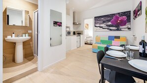 Una cuina moderna amb microones, fogó i rentapelats. Hi ha una zona de menjador amb taula preparada per a dos, i un sofà colorit al fons.