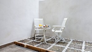 Zona d'estar exterior petita amb dues cadires blanques i una taula, disseny senzill, un plat petit de menjar i un got de suc.