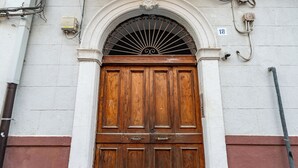 Una porta doble de fusta amb una reixa metàl·lica decorativa a la part superior, situada en un edifici amb façana blanca i vermella.
