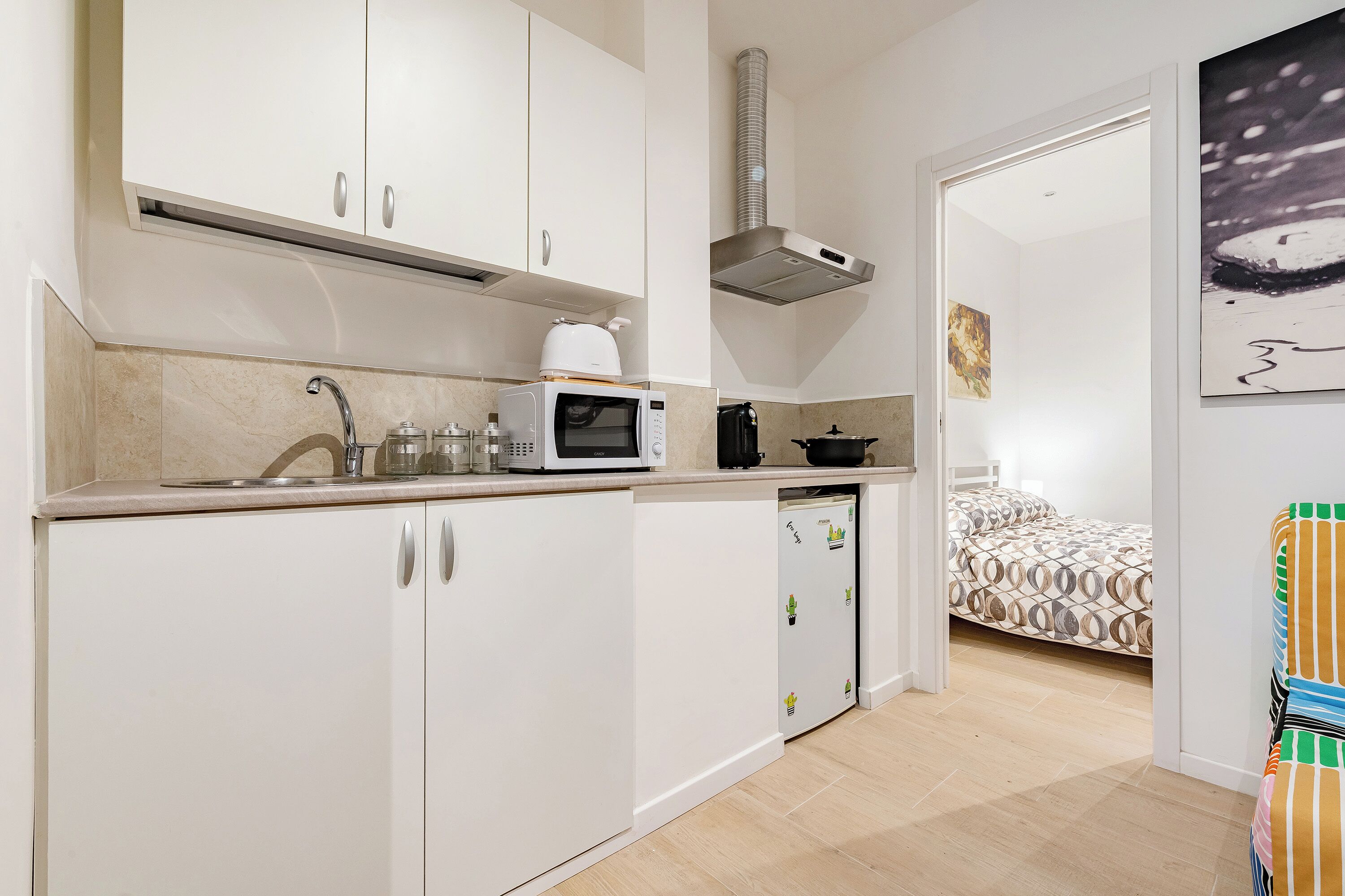 A compact kitchen with white cabinets, a microwave, a kettle, and a stove.