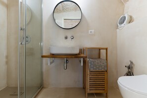 Un bagno con box doccia in vetro, un lavandino bianco con ripiano in legno, uno specchio rotondo e un water bianco.