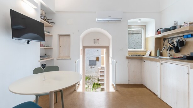 Une cuisine moderne avec des meubles blancs, un téléviseur à écran plat fixé au mur et un coin repas comprenant une table ronde et des chaises.