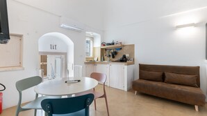 Un espace de vie compact comprenant un coin cuisine, un coin repas avec une table ronde et des chaises, et un canapé marron.