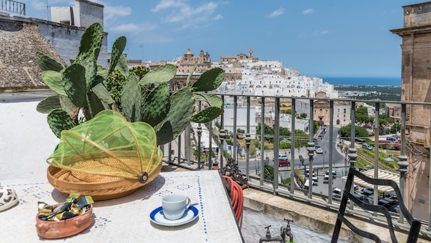 A terrace with a cactus plant, a table with a cup and saucer, and a view of a coastal town with white buildings and a clear sky. - Borgo&Mare Terrace Sant'Oronzo Palace (Ostuni)