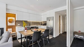 A modern kitchen with white cabinets, a wooden dining table, and black chairs. - Kiwi Studio Apartment minutes from Coronet Peak (Queenstown)