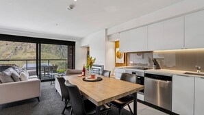 A modern kitchen with stainless steel appliances, a dining area with a wooden table and chairs, and a large window offering a view of a mountainous landscape. - Kiwi Studio Apartment minutes from Coronet Peak (Queenstown)