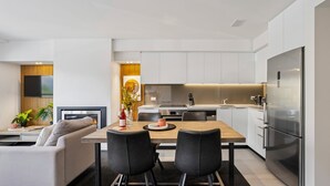A modern kitchen with white cabinets, a stainless steel refrigerator, and a dining area with a table and chairs. - Kiwi Studio Apartment minutes from Coronet Peak (Queenstown)