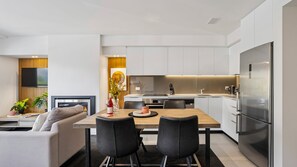 Une cuisine moderne avec des meubles blancs, un réfrigérateur en acier inoxydable et un coin repas comprenant une table et des chaises.