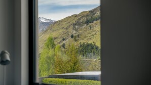 A view of a mountainous landscape through a window, featuring a solar panel array and a door frame. - Kiwi Studio Apartment minutes from Coronet Peak (Queenstown)