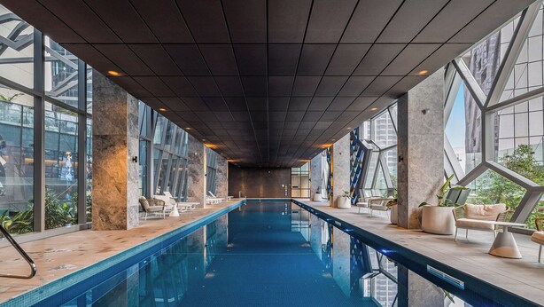 Una piscina interior moderna, de diseño largo y estrecho, con amplios ventanales y zonas de descanso a los lados.