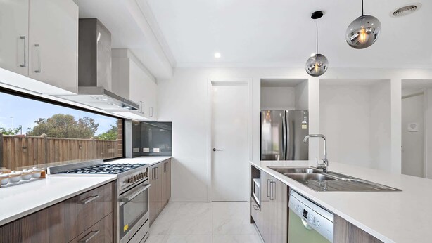 A modern kitchen with stainless steel appliances, a dishwasher, and a large window overlooking a wooden deck. - Spacious 5-Bed Home in Peaceful Point Cook (Point Cook)