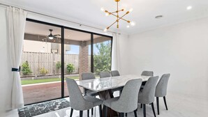 A modern dining area with a glass partition, a marble table, and grey upholstered chairs. - Spacious 5-Bed Home in Peaceful Point Cook (Point Cook)