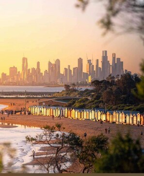 A beach with wooden beach huts and a city skyline in the background.