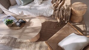 Un salon chaleureux avec un canapé, une couverture blanche et moelleuse, un plaid tricoté, une table d’appoint en bois et un tapis tissé.