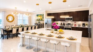 A modern kitchen with dark wood cabinets, stainless steel appliances, and a central island with bar stools. - 27-bedroom luxury villa near Disney (Kissimmee)