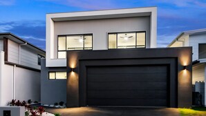 Een modern huis met twee verdiepingen, een donkere garagepoort, grote ramen en buitenverlichting.