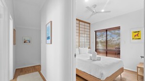 Un dormitorio con cama, ventilador de techo, ventana con persianas y una mesita de noche pequeña.