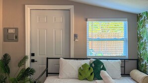 Ein Schlafzimmer mit Bett, Fenster mit Jalousien, Tür und einem an der Wand befestigten Thermostat.