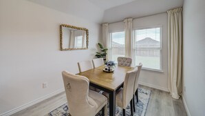 A dining area with a wooden table, four chairs, a mirror, and a window with curtains.